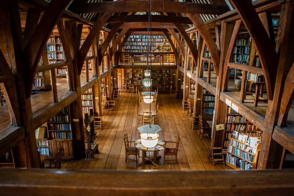 Interior of a traditional library with wooden beams, high ceilings, and shelves filled with books on two levels.