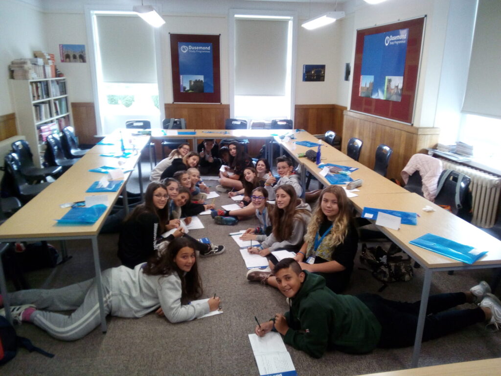 Students lying on the classroom floor and working in groups on their writing tasks during a Dusemond study session.
