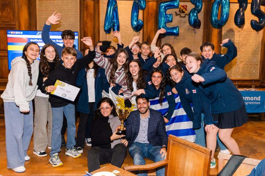 Group of smiling students and teachers celebrating with trophy and certificate under ACE 2025 decorations.