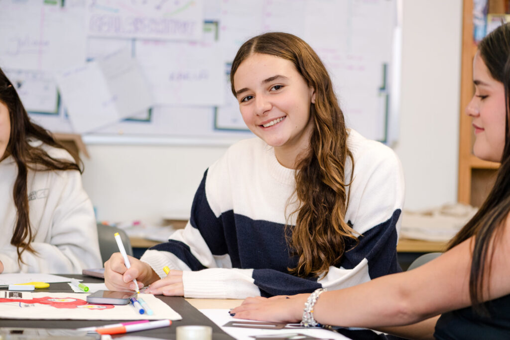 Girl smiling while drawing with markers during a classroom art activity.