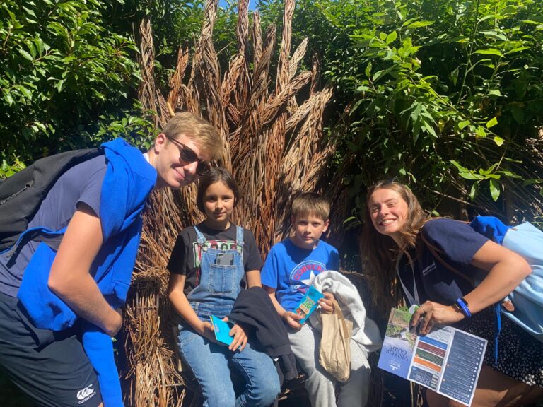 Two Dusemond leaders smiling with two young students seated on a wooden throne made of branches in a garden setting